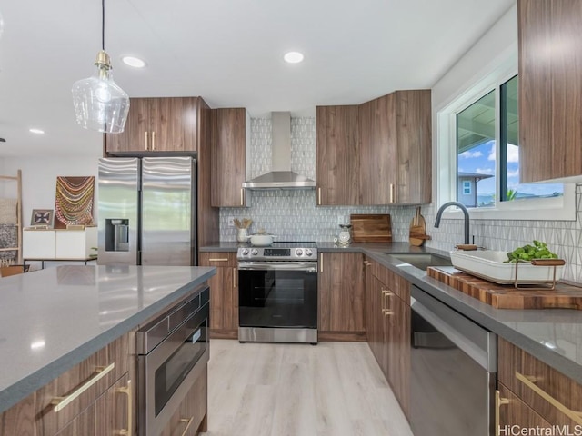 kitchen featuring a sink, wall chimney range hood, brown cabinets, and stainless steel appliances