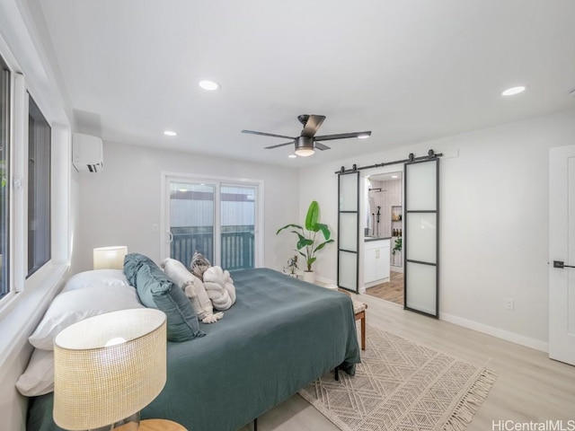 bedroom featuring light wood-style flooring, access to outside, a wall unit AC, recessed lighting, and a barn door