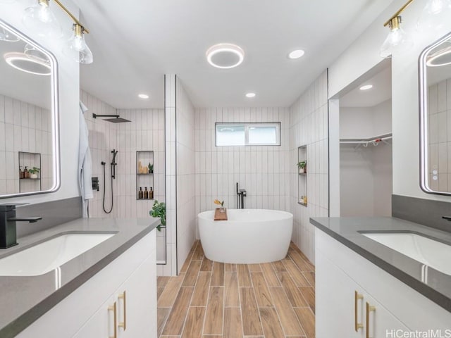 bathroom with a freestanding bath, tile walls, wood finish floors, and a sink