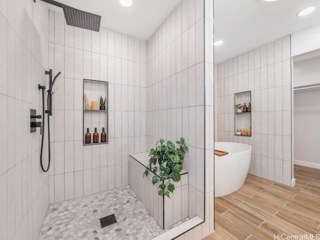 bathroom featuring wood finish floors, walk in shower, a freestanding bath, recessed lighting, and tile walls