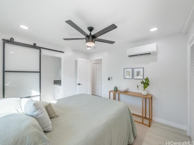 bedroom featuring baseboards, light wood-type flooring, a barn door, a closet, and a wall mounted AC