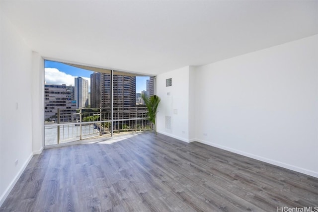 empty room featuring a city view, wood finished floors, baseboards, and expansive windows