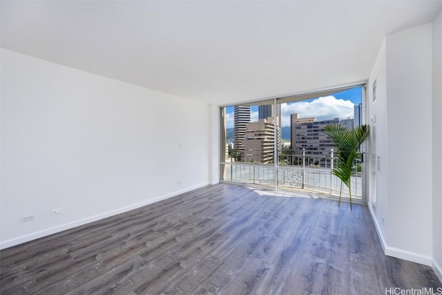 unfurnished room featuring a wall of windows, baseboards, wood finished floors, and a view of city