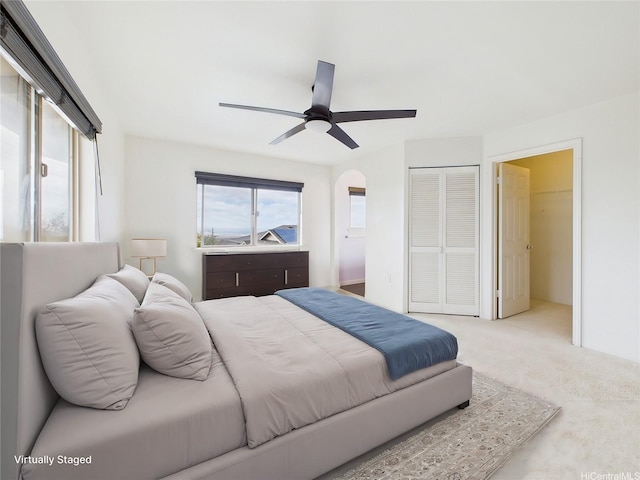 bedroom with a closet, ceiling fan, arched walkways, and carpet flooring