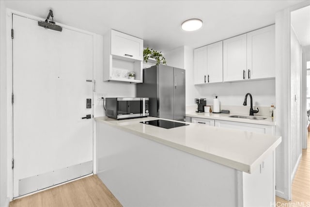 kitchen featuring light wood finished floors, open shelves, appliances with stainless steel finishes, white cabinetry, and a sink