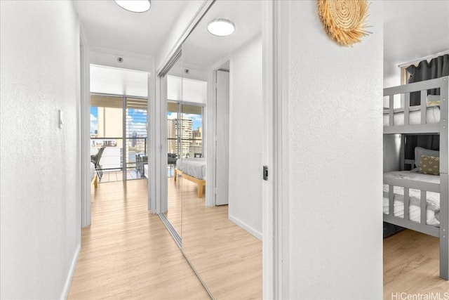 corridor featuring baseboards, a textured wall, and light wood-style floors