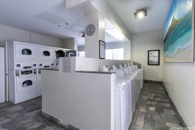 community laundry room with stacked washer and dryer, stone finish floor, baseboards, and separate washer and dryer