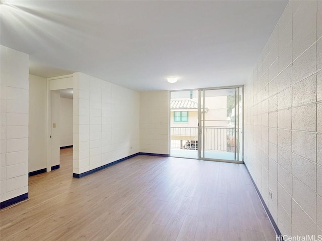 empty room featuring expansive windows, wood finished floors, and tile walls