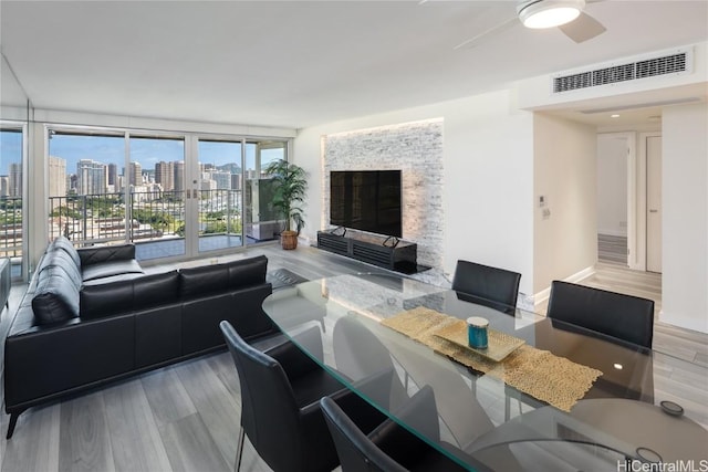 living area featuring wood finished floors, visible vents, a fireplace, ceiling fan, and floor to ceiling windows