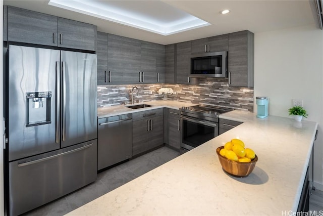 kitchen featuring a sink, stainless steel appliances, a raised ceiling, and backsplash