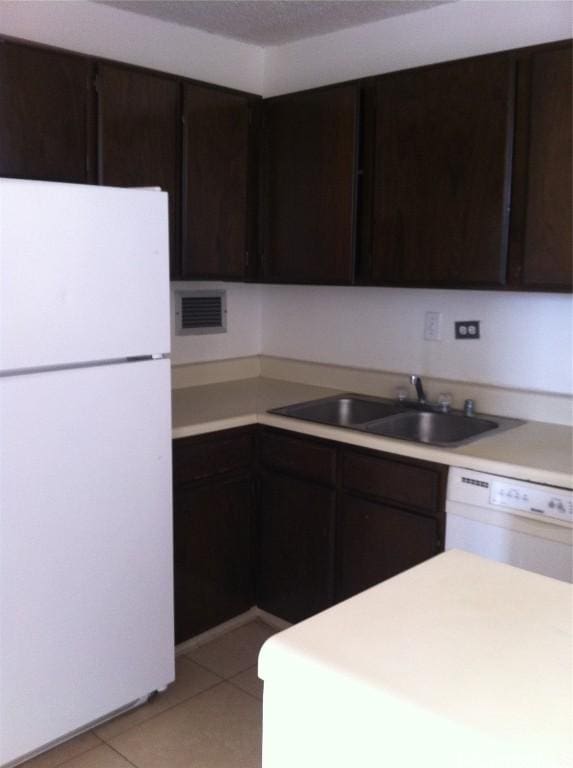 kitchen with light countertops, visible vents, a sink, dark brown cabinetry, and white appliances