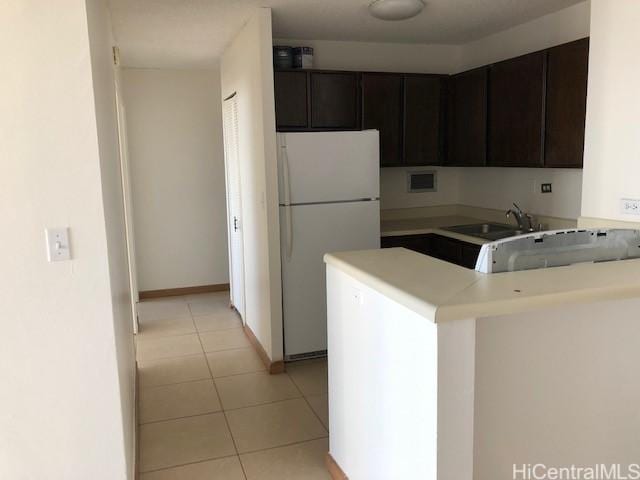 kitchen featuring light tile patterned floors, a peninsula, a sink, light countertops, and freestanding refrigerator