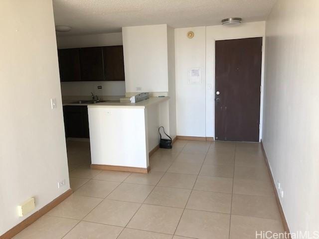 kitchen featuring light tile patterned floors, a textured ceiling, a sink, baseboards, and light countertops