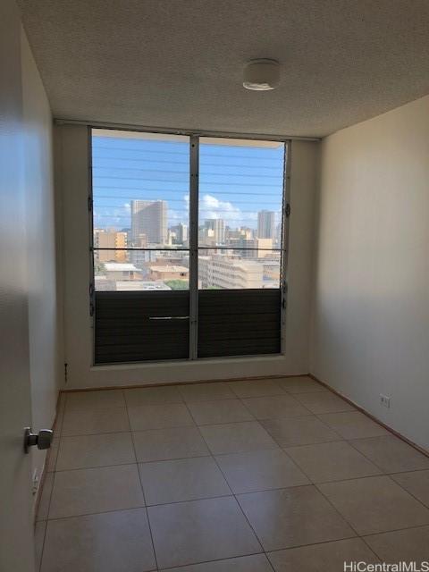 empty room featuring a city view, a textured ceiling, and light tile patterned floors