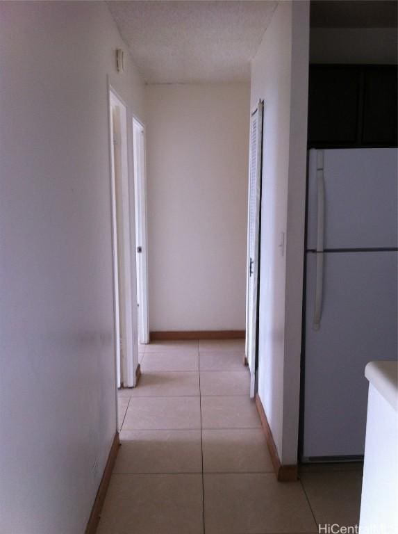 hallway with light tile patterned floors, baseboards, and a textured ceiling