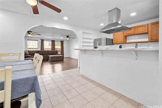 kitchen with a kitchen bar, island exhaust hood, arched walkways, and freestanding refrigerator