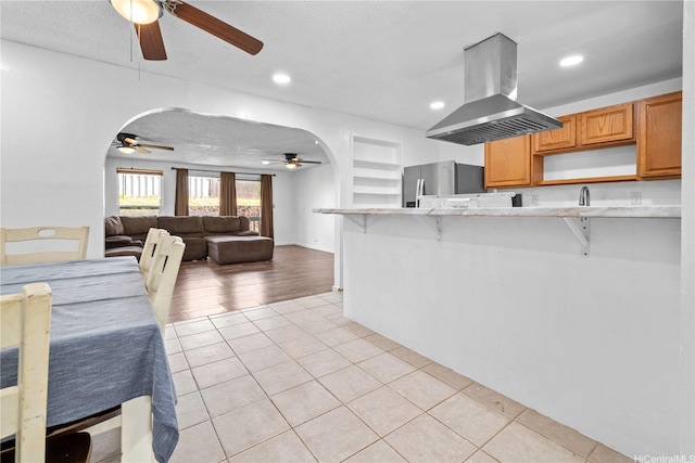 kitchen featuring ceiling fan, stainless steel fridge, a breakfast bar area, light tile patterned floors, and island range hood