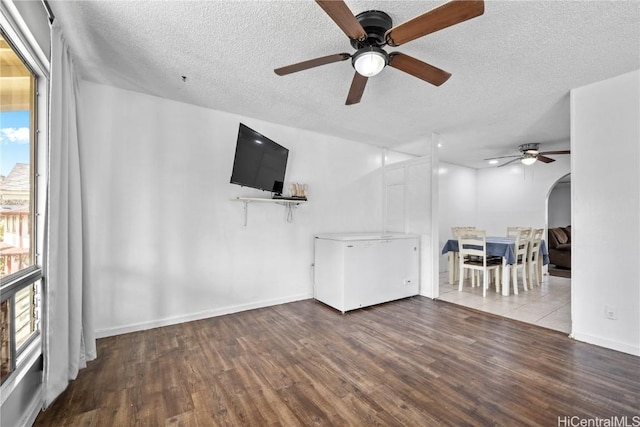 unfurnished living room featuring arched walkways, a textured ceiling, baseboards, and wood finished floors