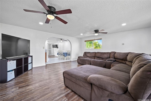 living area with arched walkways, ceiling fan, and a textured ceiling