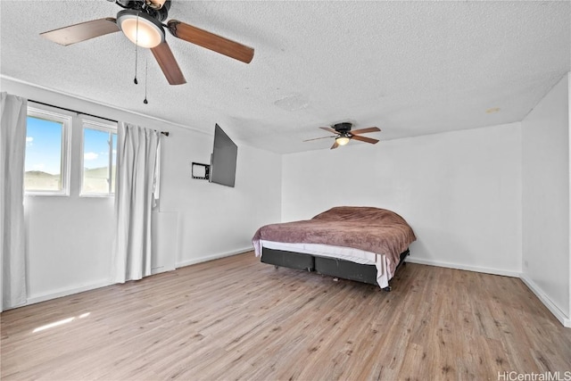 bedroom with light wood-type flooring, ceiling fan, baseboards, and a textured ceiling