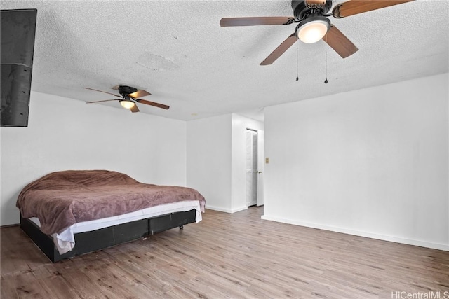 bedroom with ceiling fan, a textured ceiling, baseboards, and wood finished floors