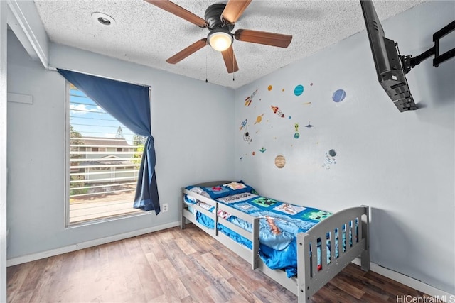 bedroom with a textured ceiling, ceiling fan, wood finished floors, and baseboards