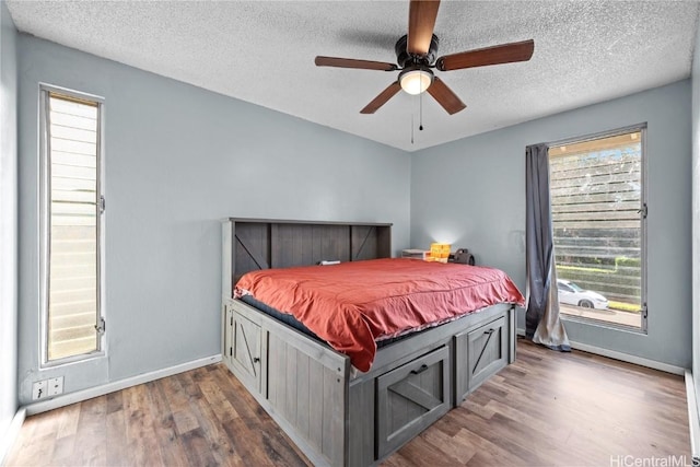 bedroom with dark wood-type flooring, a textured ceiling, baseboards, and a ceiling fan