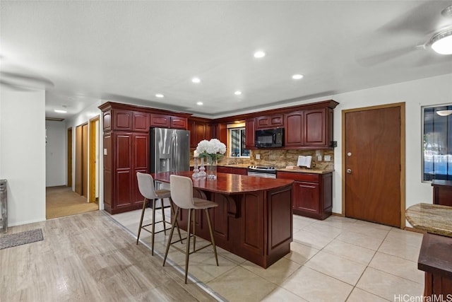 kitchen featuring a kitchen bar, a center island, stainless steel appliances, reddish brown cabinets, and decorative backsplash