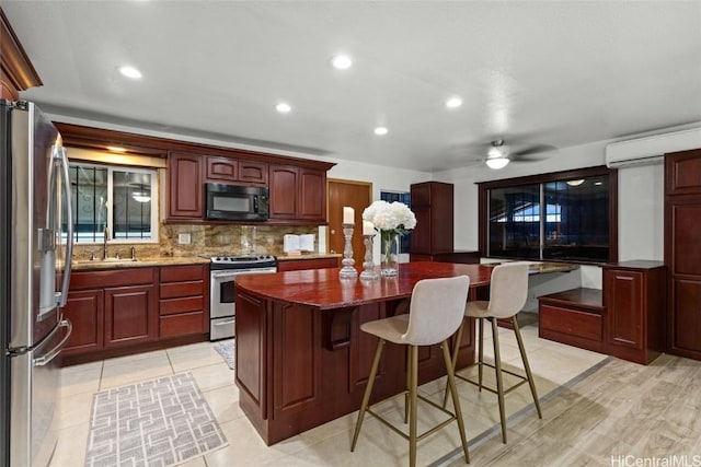 kitchen featuring a center island, reddish brown cabinets, appliances with stainless steel finishes, a breakfast bar area, and decorative backsplash