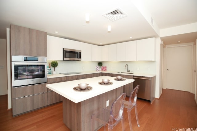 kitchen featuring visible vents, a sink, stainless steel appliances, light wood finished floors, and light countertops