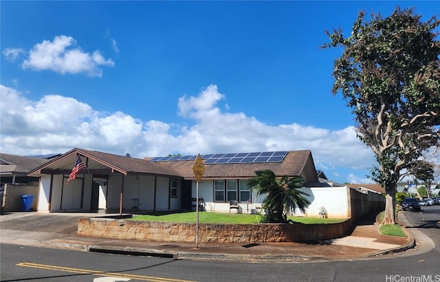 ranch-style house featuring an attached carport, solar panels, fence, driveway, and a front lawn