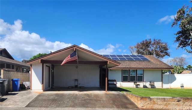 ranch-style house with solar panels, concrete driveway, an attached carport, fence, and a front lawn