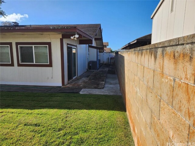 view of side of home with a yard, central AC unit, and fence