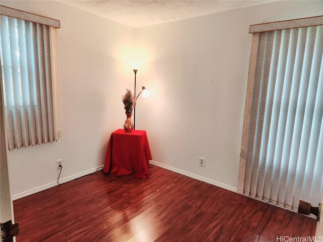 empty room with a textured ceiling, wood finished floors, and baseboards