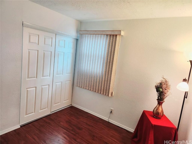 unfurnished bedroom with a closet, a textured ceiling, baseboards, and wood finished floors