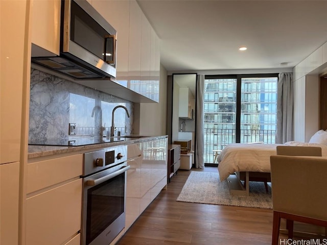 kitchen with a sink, stainless steel appliances, dark wood-type flooring, white cabinetry, and backsplash