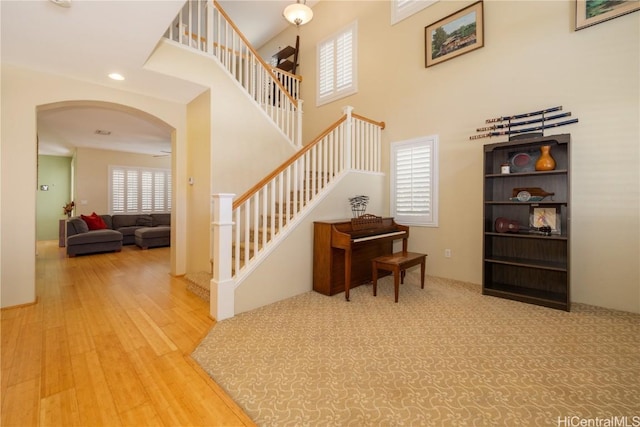 staircase with arched walkways, a high ceiling, wood finished floors, and recessed lighting