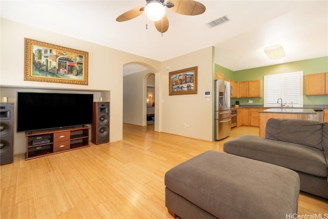 living area featuring arched walkways, ceiling fan, visible vents, and light wood-style floors