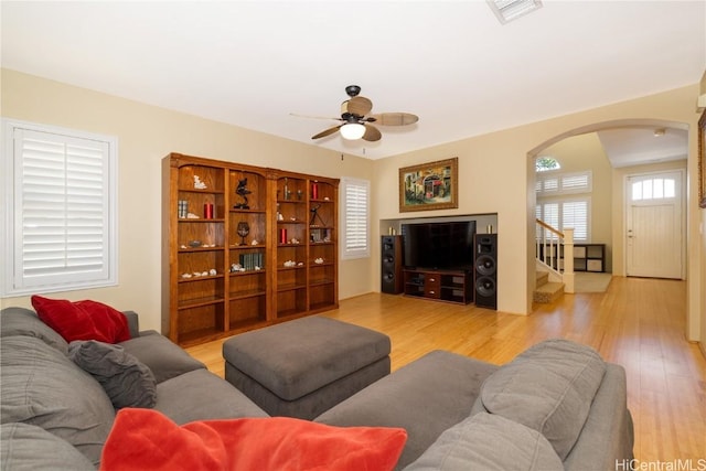 living room with visible vents, arched walkways, a ceiling fan, wood finished floors, and stairs