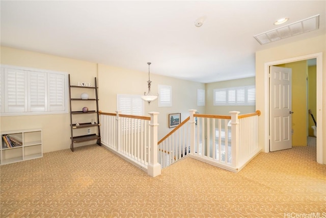 hallway with carpet floors, visible vents, and an upstairs landing