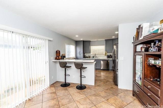 kitchen with a breakfast bar area, gray cabinetry, stainless steel appliances, a sink, and light countertops