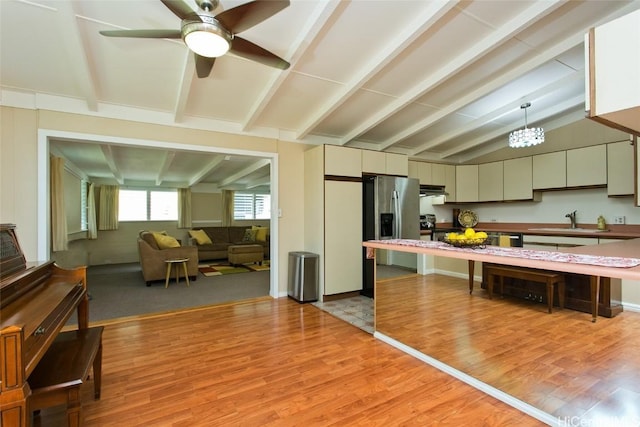 kitchen featuring a sink, under cabinet range hood, stainless steel fridge with ice dispenser, light wood finished floors, and vaulted ceiling with beams