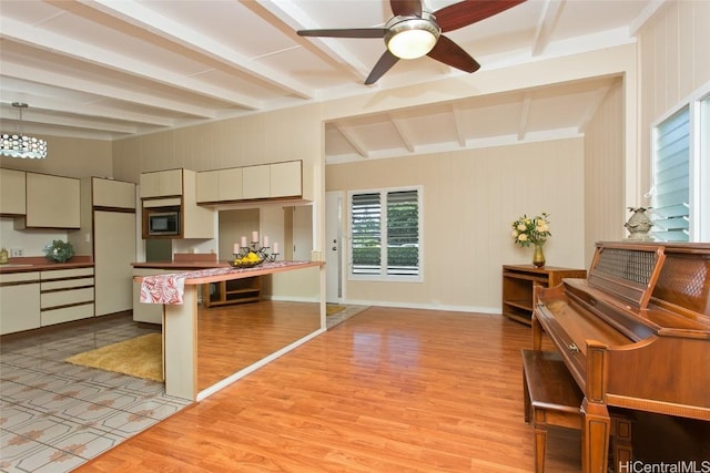 kitchen with beam ceiling, stainless steel microwave, a peninsula, and light wood-style floors