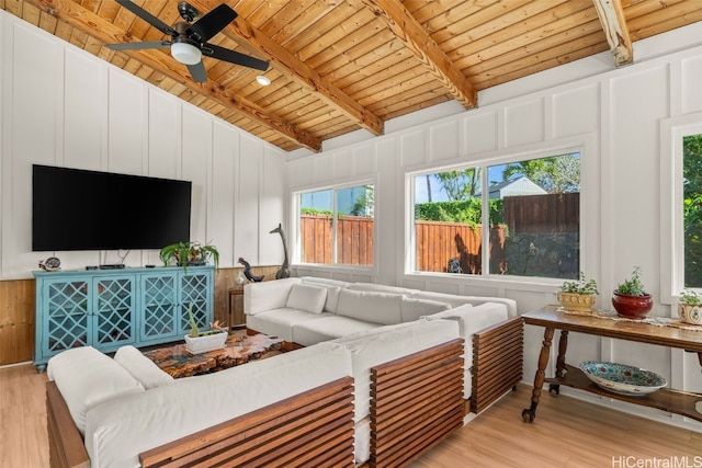 living area featuring a ceiling fan, lofted ceiling with beams, light wood-style floors, a decorative wall, and wood ceiling