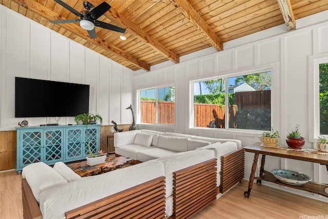 living area featuring a decorative wall, light wood-style floors, ceiling fan, vaulted ceiling with beams, and wood ceiling