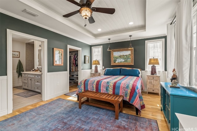 bedroom featuring visible vents, a walk in closet, a tray ceiling, light wood-style floors, and wainscoting