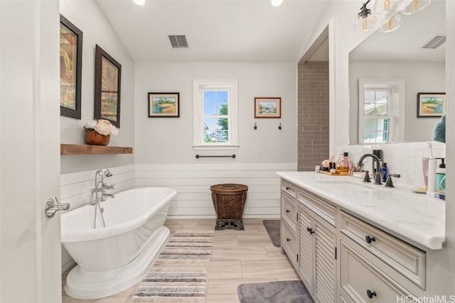 bathroom featuring vanity, a freestanding tub, visible vents, and a wainscoted wall