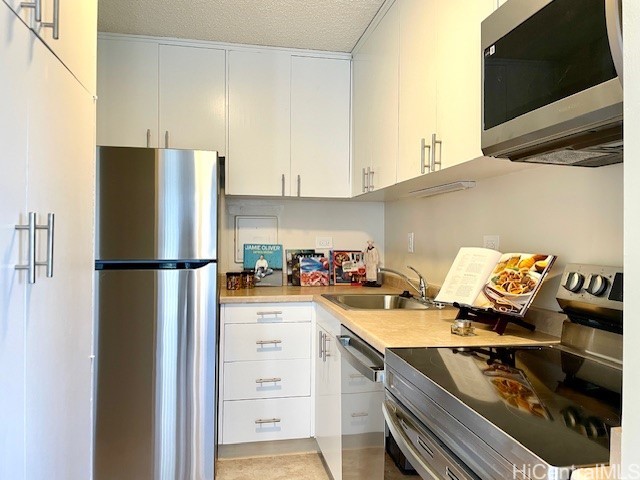 kitchen with light countertops, appliances with stainless steel finishes, white cabinetry, a sink, and a textured ceiling