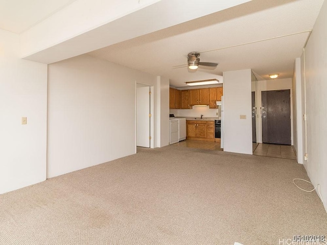 unfurnished living room featuring a sink, washing machine and clothes dryer, a ceiling fan, and light colored carpet