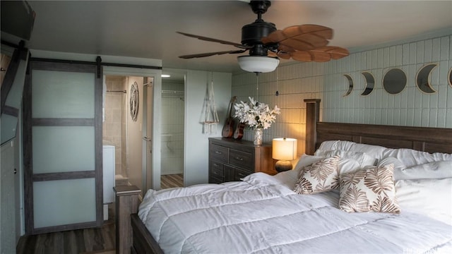 bedroom with ceiling fan, a barn door, wood finished floors, and connected bathroom